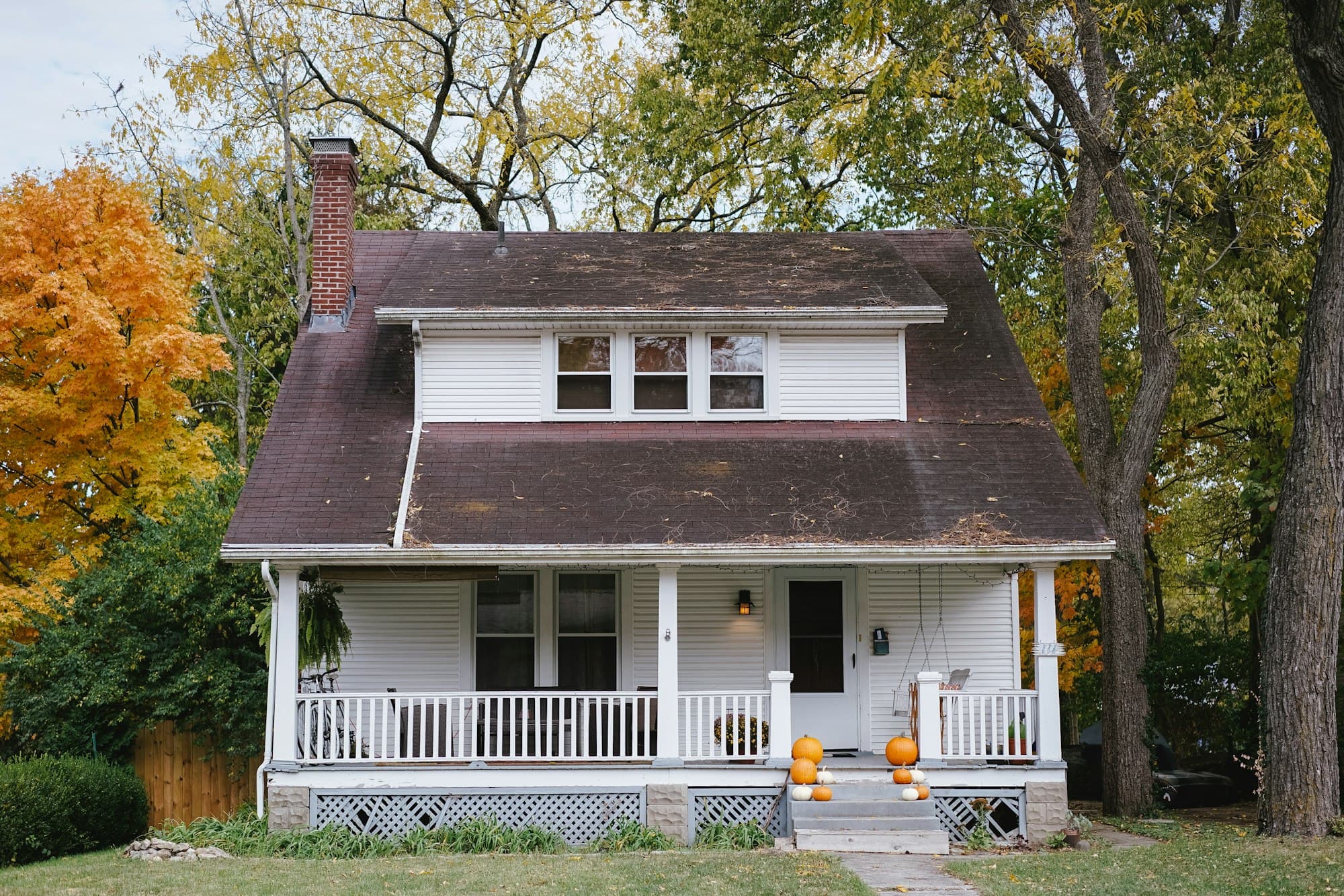 A white bungalow with a front porch on a tree-lined street in autumn